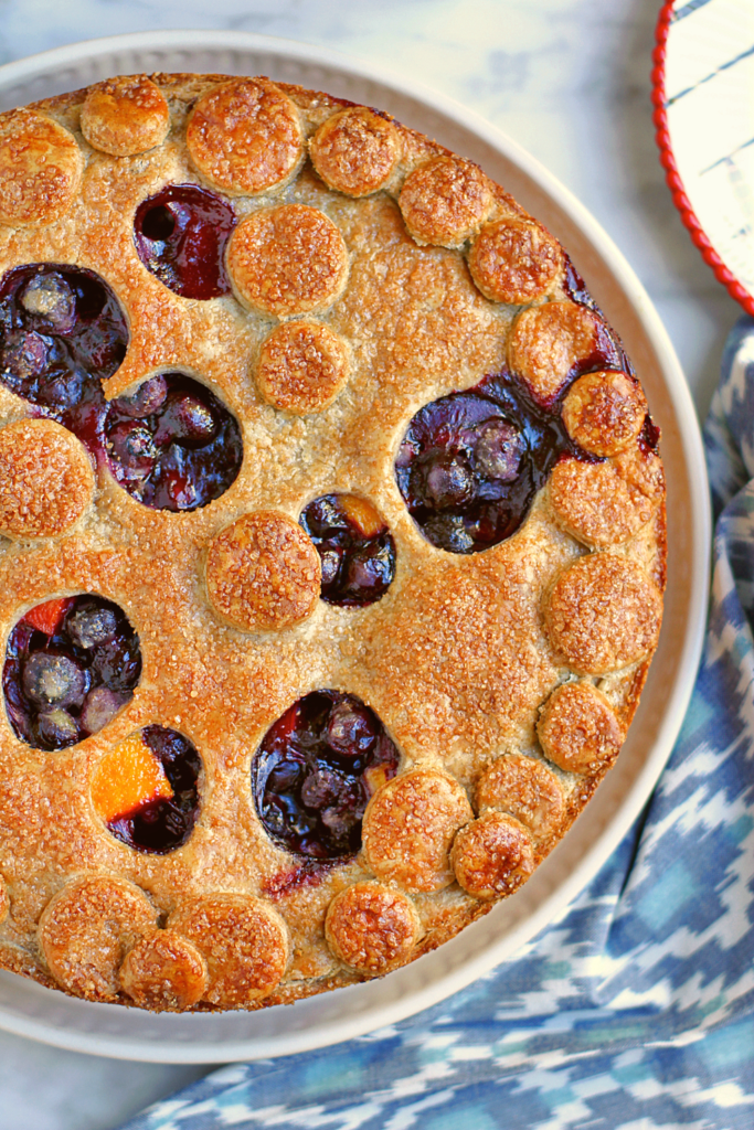 Close-up image of peach and blueberry pie with a rye crust.
