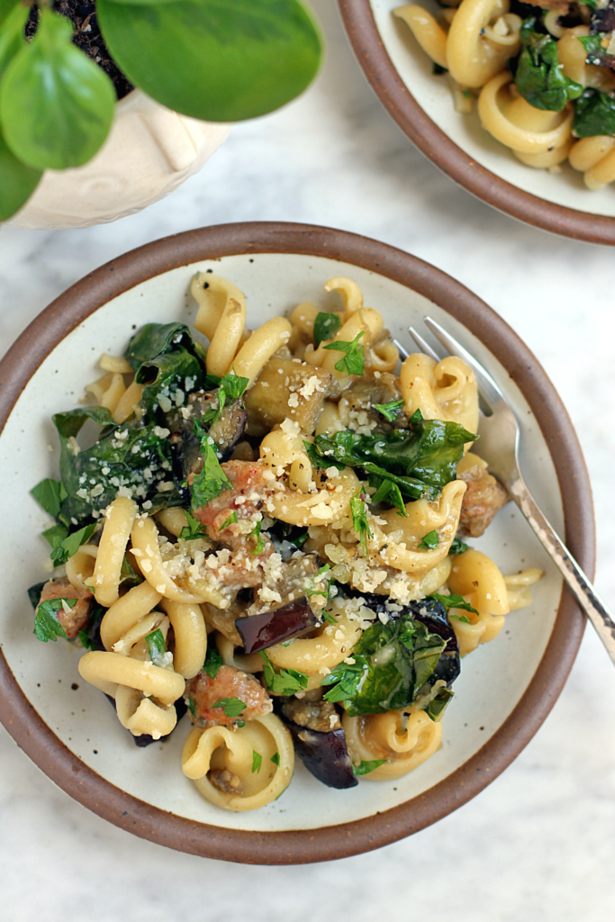 Close-up image of pasta with eggplant, kale and sausage.