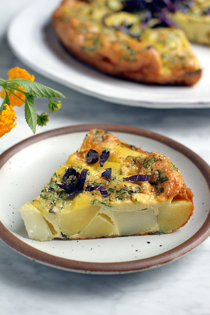 Image of a slice of potato frittata with cheese and herbs.