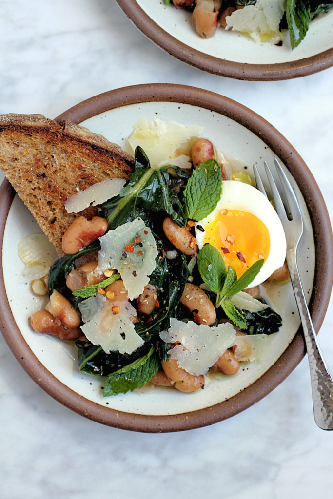 Close-up image of brothy beans and greens on toast.