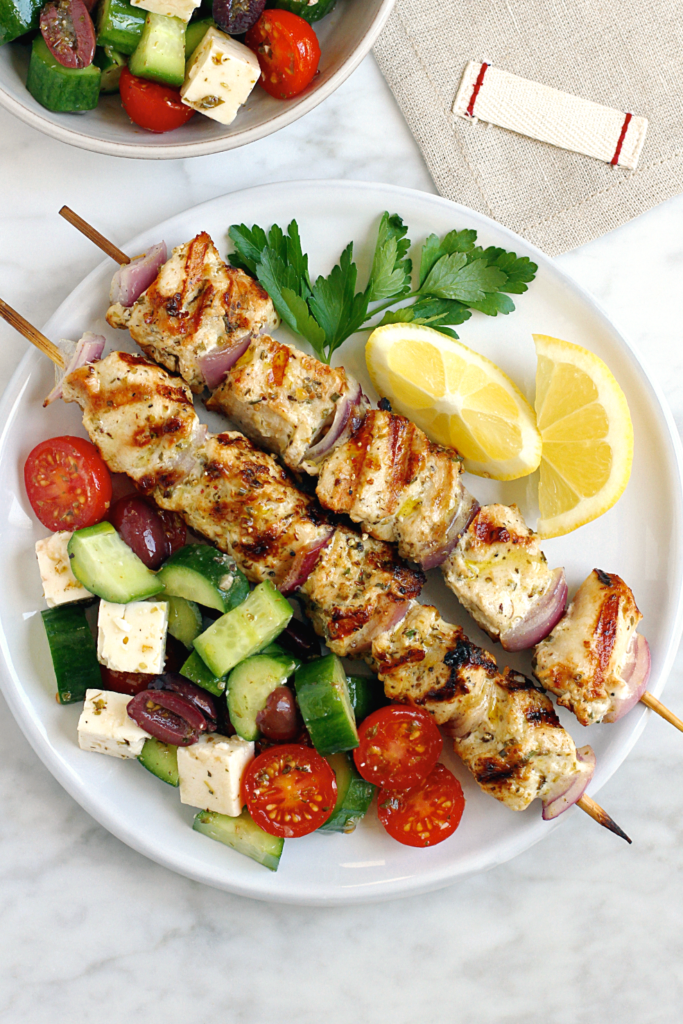 Close-up image of grilled Greek chicken kebabs with cucumber, tomato and Feta salad. 
