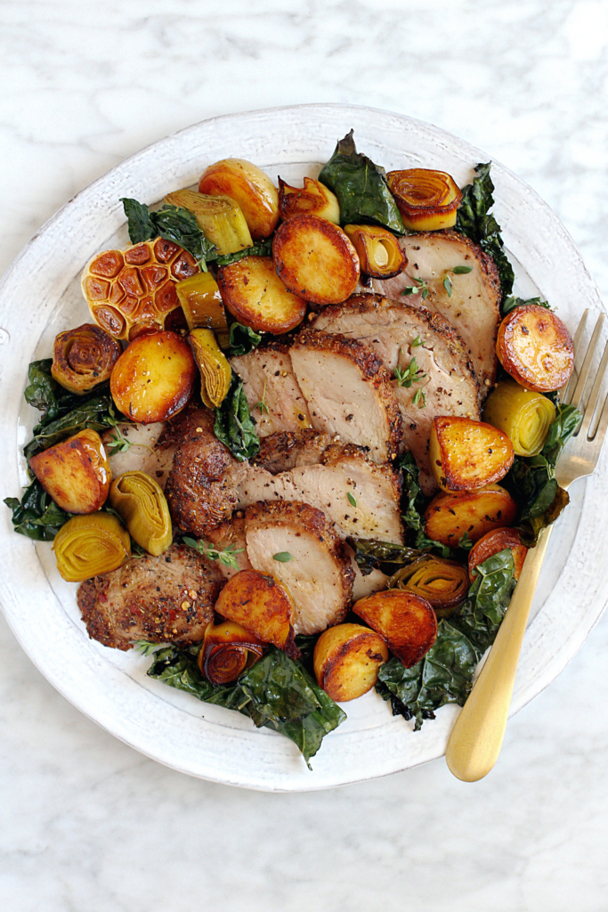 Close-up image of roasted pork loin with potatoes and kale.